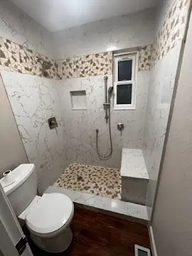 Walk-in shower with marble-look tile, pebble floor and mosaic border